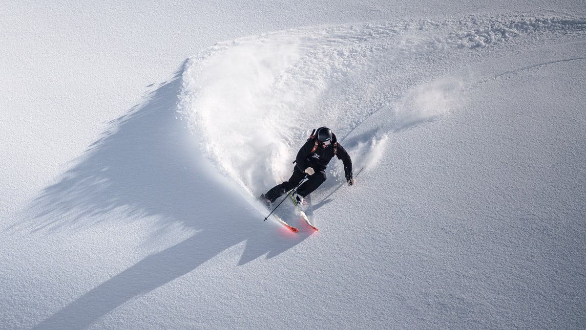 A skier carves through fresh powder snow in Colere, Italy, showcasing winter sports excitement.